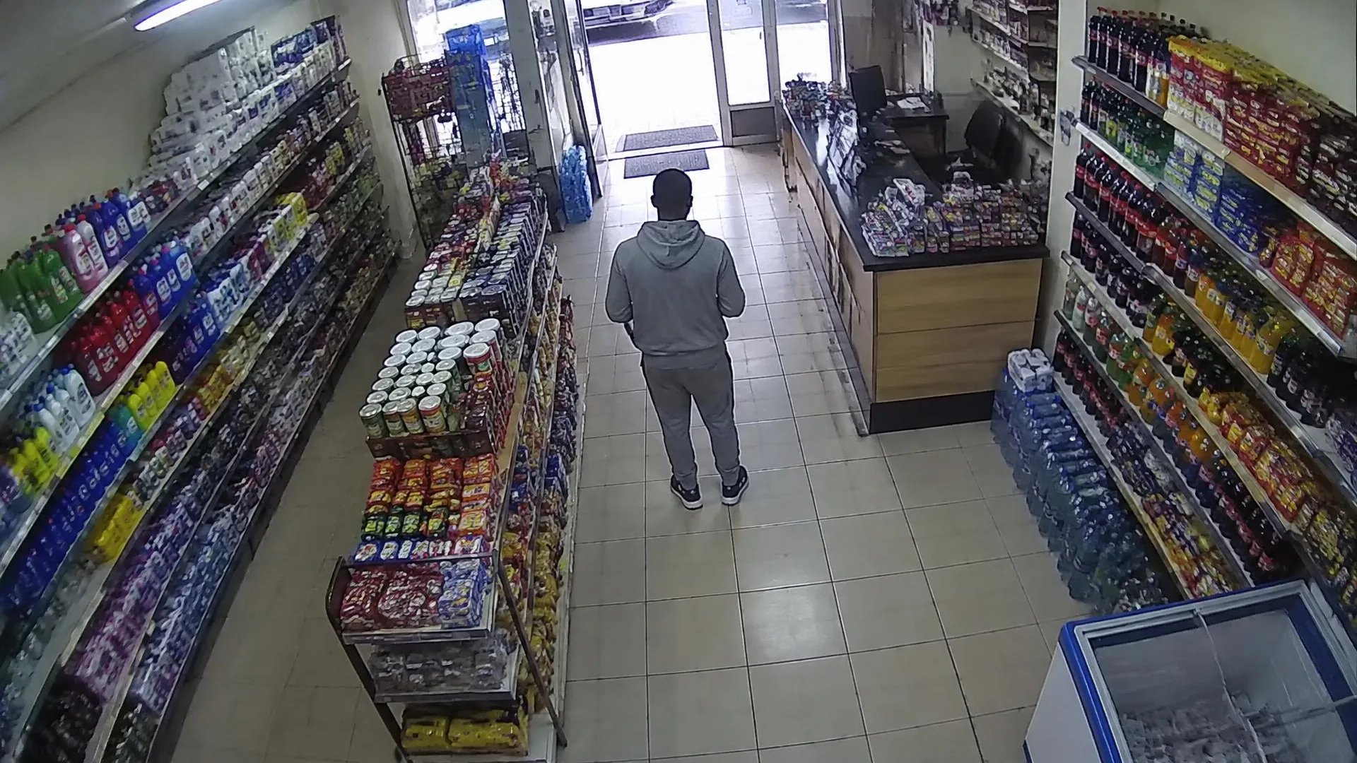 High corner camera view of a Nairobi convenience shop with a customer seen from behind in the central aisle.